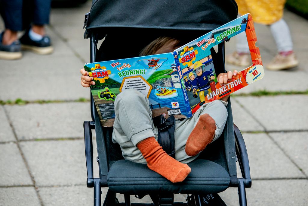 Barn sitter i barnevogn og leser